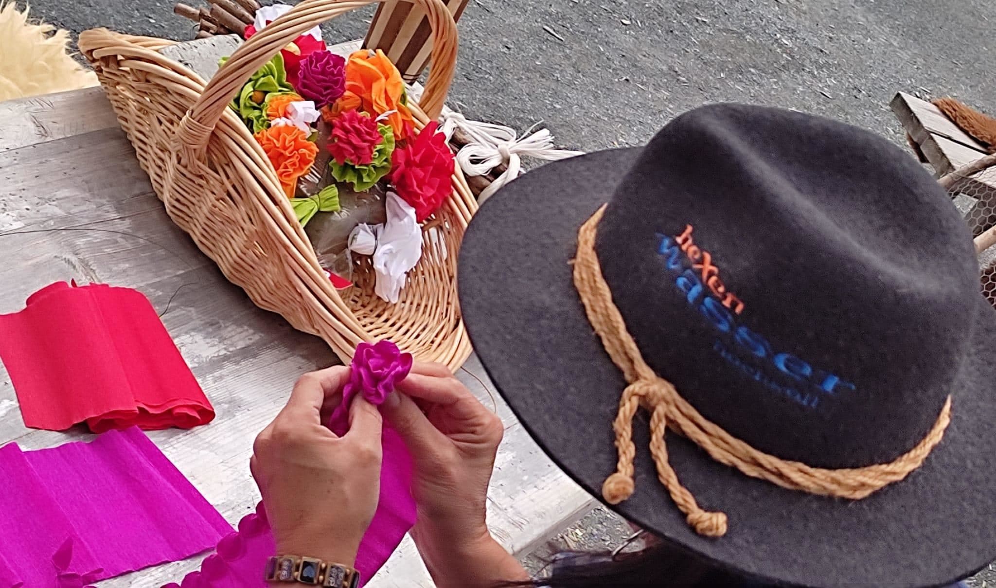 Eine Person bastelt Blumen aus buntem Stoff. Im Hintergrund ist ein Korb mit bereits fertiggestellten Blumen zu sehen.